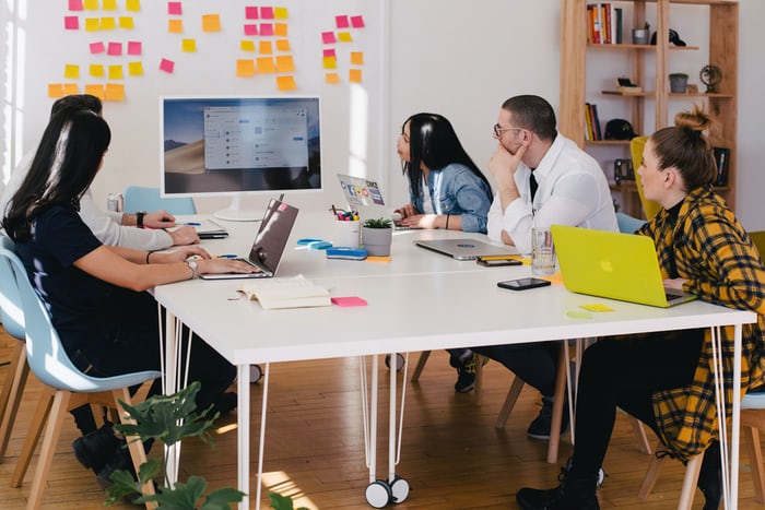 5 adults in a meeting room looking at a desktop screen.