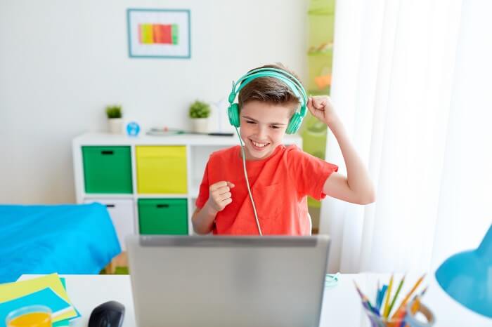 A kid with a headset looking at the computer screen with a smile on his face